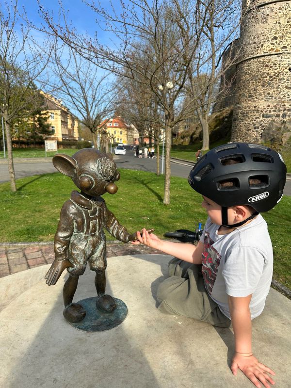 Chlapec s helmou na hlavě podává ruku bronzové soše Hurvínka.