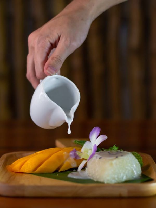Ruka nalévá kokosové mléko na mango sticky rice.