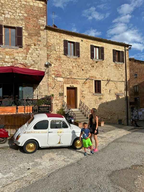 Žena a chlapec stojí vedle bílého Fiata před italským domkem.