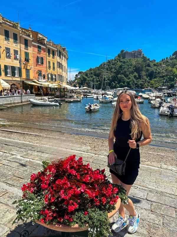 žena stojí vedle květináče s červenými květy v Portofinu, lodě a domky v pozadí