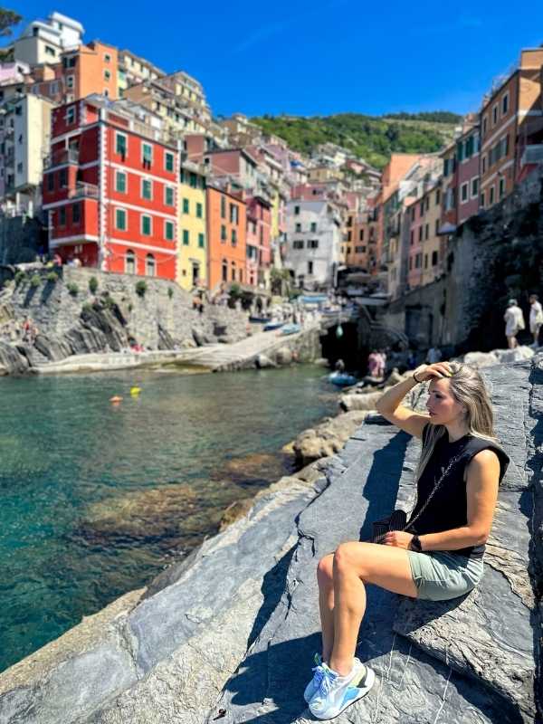 žena sedí na kameni, v pozadí barevné domky Cinque Terre