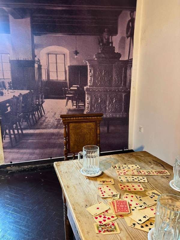 stůl s rozházenými hracími kartami, půllitr a za ním tapeta připomínající minulost