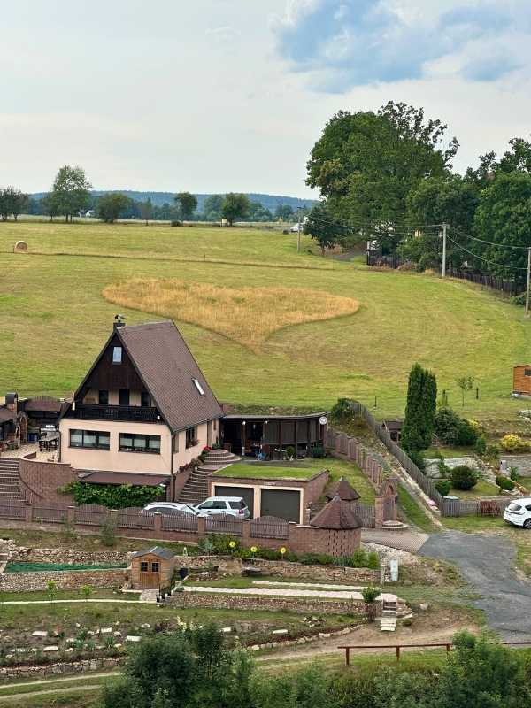 útulná chatka uprostřed polí a lesa, v poli se obilí vysekalo do tvaru srdce