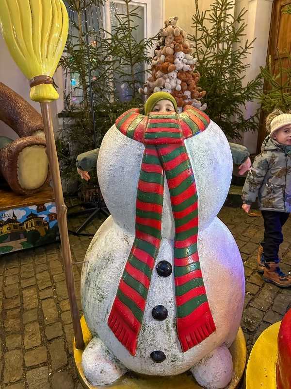 Chlapec stojí za postavou sněhuláka, kolem vánoční atmosféra.