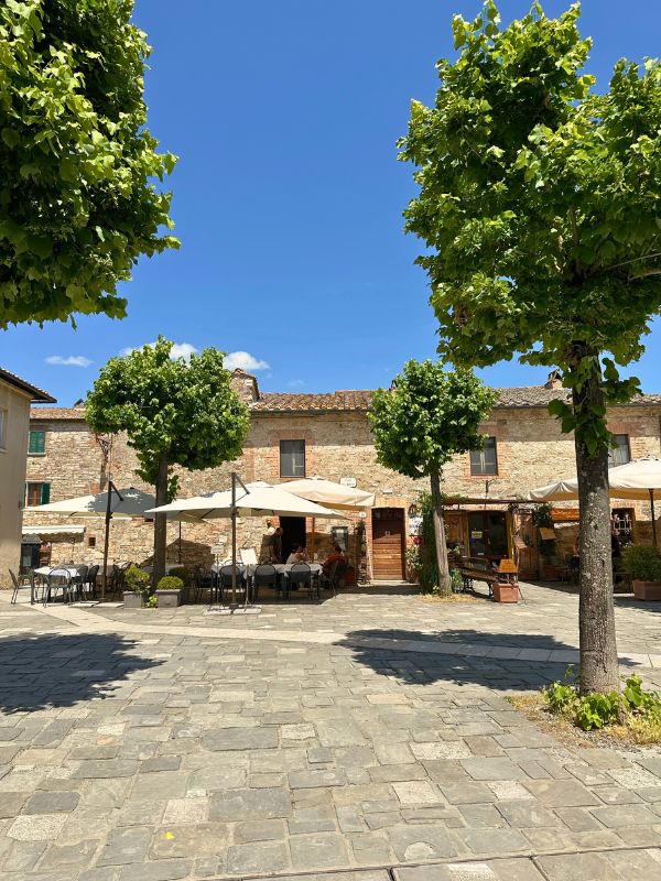 Klasický italský domek na náměstíčku v Bagno Vignoni obklopený zelenými stromy.