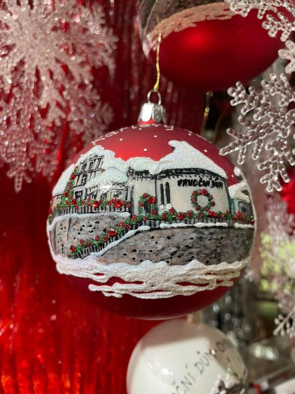 Červená ozdoba s namalovaným vánočním domem.