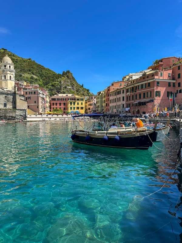 loďka v průzračně čisté vodě, v pozadí barevné domky Cinque Terre, modrá obloha