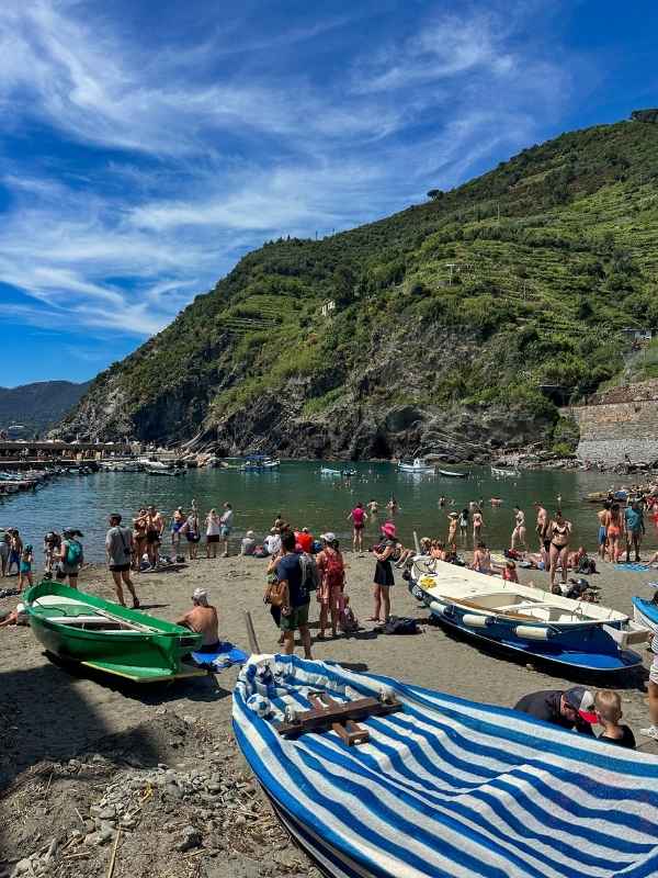 malá pláž s lidmi, loděmi, zelenými kopci a modrou oblohou