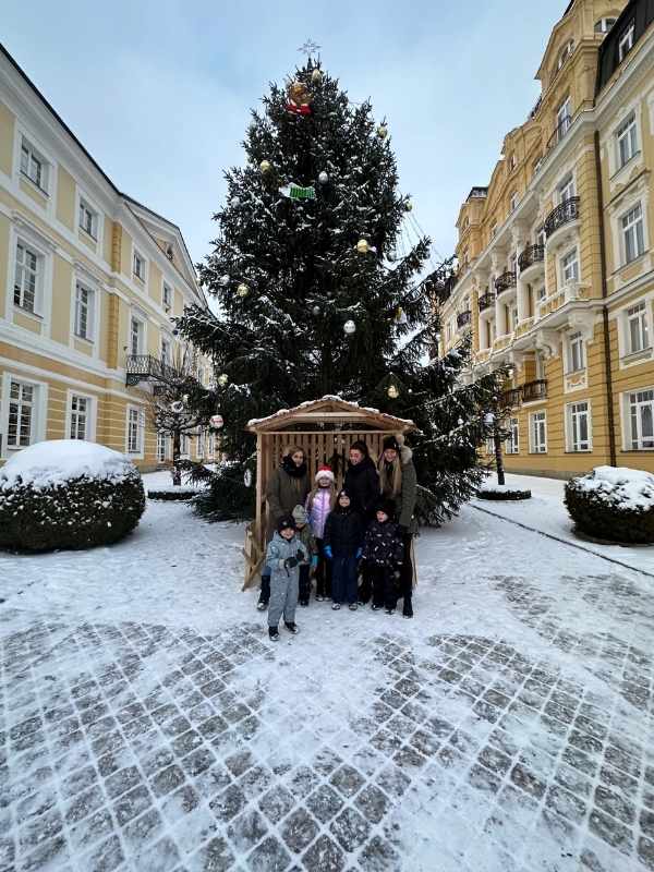 Vánoční stromeček na náměstíčku ve Františkových Lázních obklopený žlutými domy s lidmi pózujícími před ním.