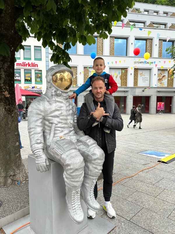 Muž drží chlapce na ramenou vedle sochy astronauta na náměstí v Lichtenštejnsku.