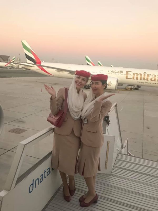 Dvě letušky pózují při nástupu do letadla, v pozadí další letadlo Emirates
